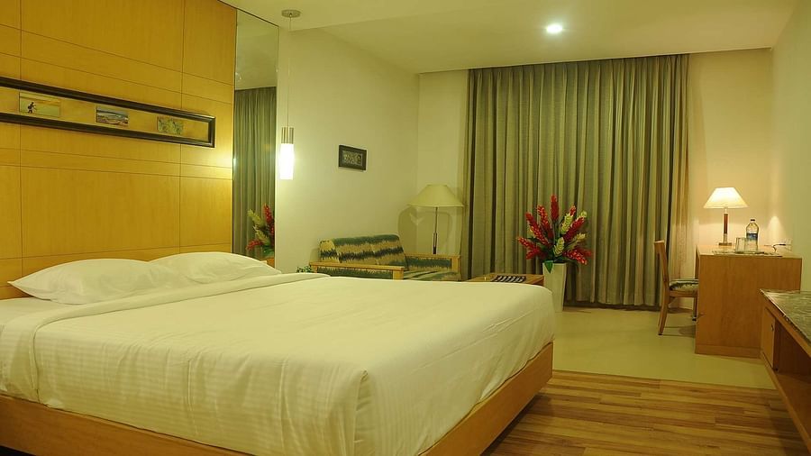 Side interior view of a Executive Room at Dhanalakshmi Srinivasan Hotels, Perambalur, showcasing a bed, side table, and seating area.