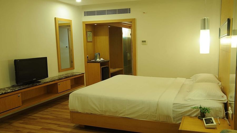 Interior view of Executive Room at Dhanalakshmi Srinivasan Hotels, Perambalur featuring a King bed, furniture, and a mirror. 