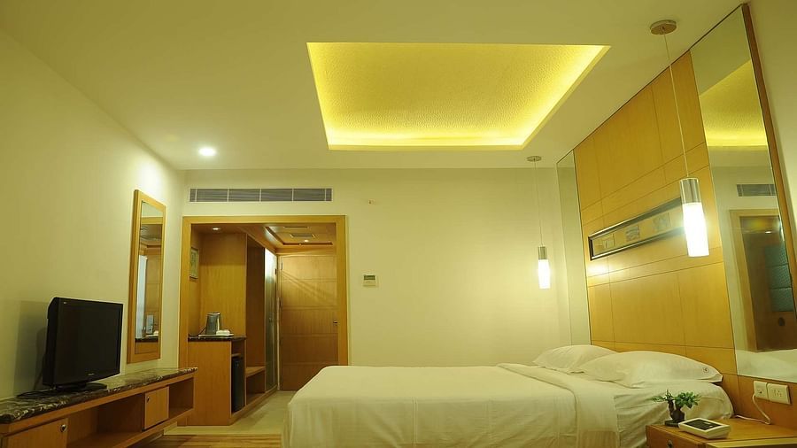 Side view of Executive Room at Dhanalakshmi Srinivasan Hotels, Perambalur featuring a King bed, furniture, and a window view. 