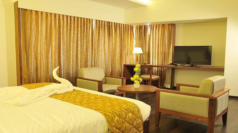 Interior view of a Executive Room at Dhanalakshmi Srinivasan Hotels, Perambalur, showcasing a bed, side table, and seating area.