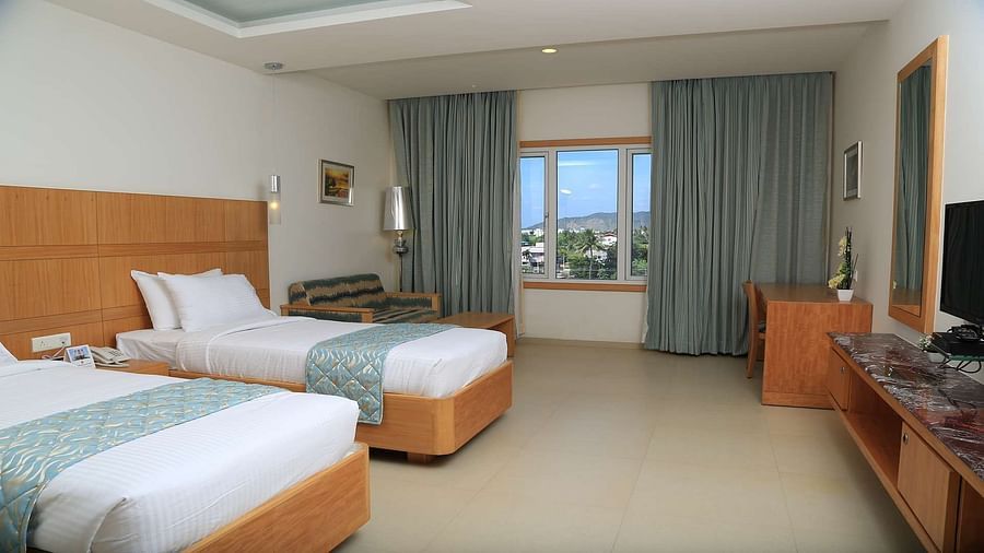 Executive Room at Dhanalakshmi Srinivasan Hotels, Perambalur featuring twin beds, furniture, and a window view. 