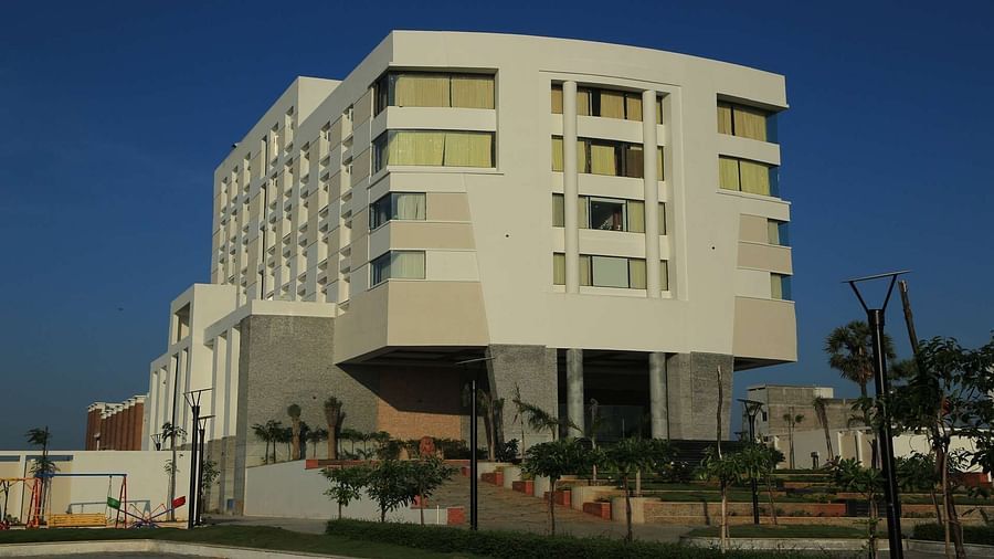 A modern white multi-storey hotel building against a blue sky, offering a luxurious stay in a prime location.- Dhanalakshmi Srinivasan Hotels, Perambalur
