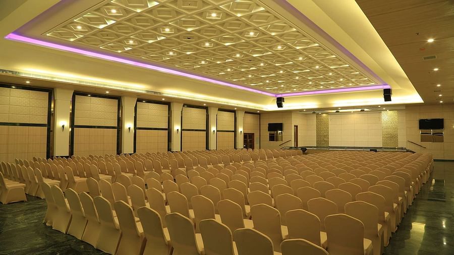 Side view of DS Mahal Hall at Dhanalakshmi Srinivasan Hotels, Perambalur with  chairs arranged in theatre seating and chandelier on top. 