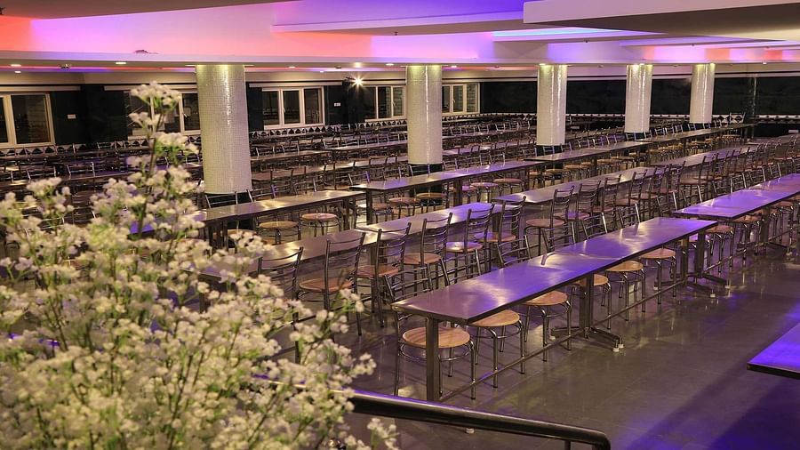 Dining area of DS Mahal Hall at Dhanalakshmi Srinivasan Hotels, Perambalur featuring tables and chairs set up with flower pots on the side.