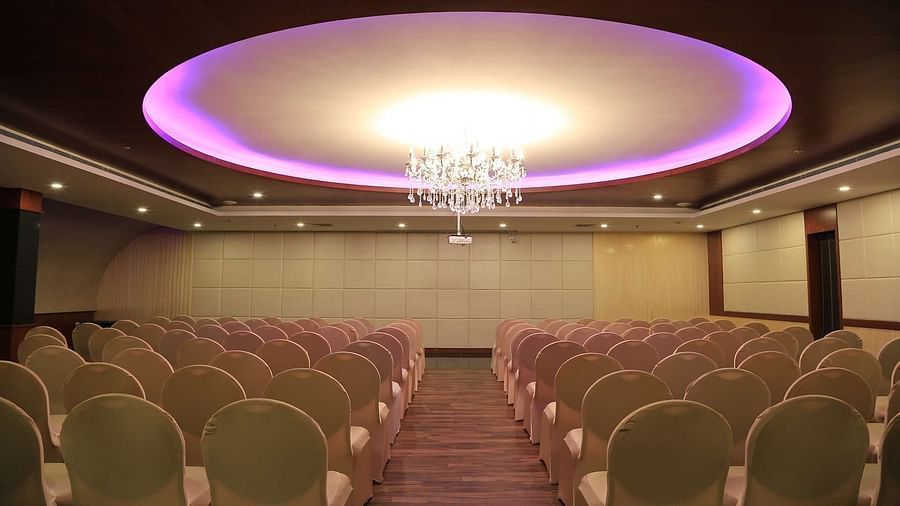 Orchid Hall at Dhanalakshmi Srinivasan Hotels, Perambalur with  chairs arranged in theatre seating and chandelier on top. 