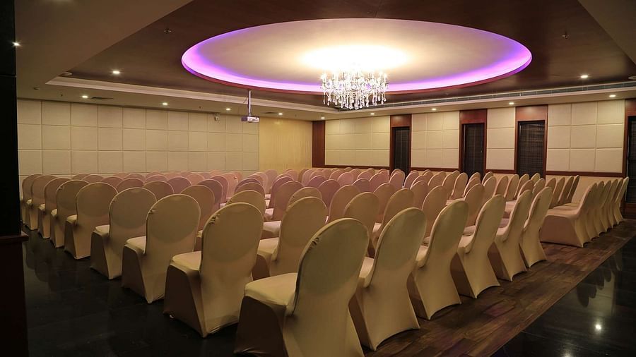 Side view of Orchid Hall at Dhanalakshmi Srinivasan Hotels, Perambalur with  chairs arranged in theatre seating and chandelier on top. 