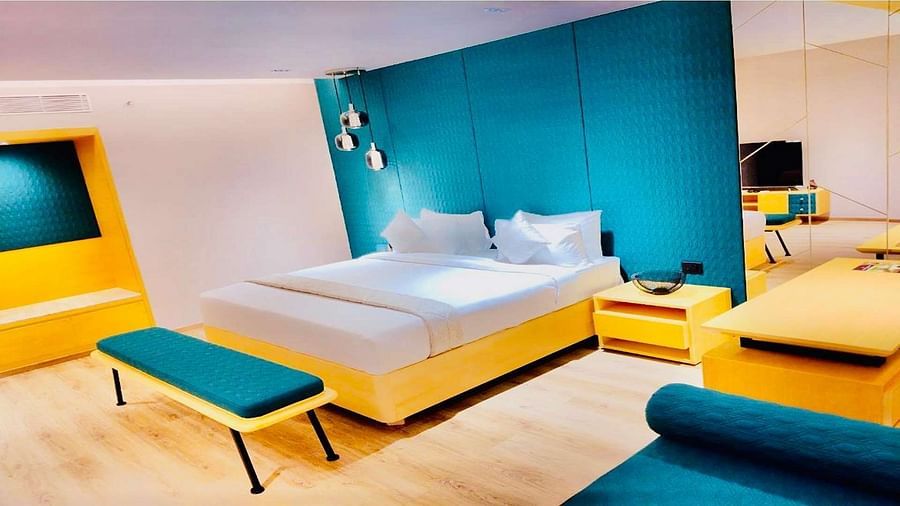 Side view of a Presedential Suite featuring a King size bed with white linens and decorative swans, a green accent wall, yellow furniture, and hardwood floors. Dhanalakshmi Srinivasan Hotels, Perambalur