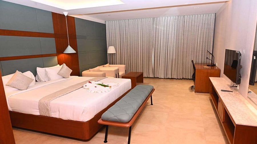 Side view of a Executive Room at Dhanalakshmi Srinivasan Hotels, Perambalur, showcasing a bed, side table, and seating area.