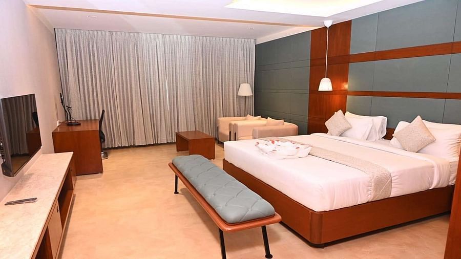 A Executive Suite at Dhanalakshmi Srinivasan Hotels, Perambalur featuring a neatly made bed with white linens and pillows, a wooden headboard, and a desk with a chair.