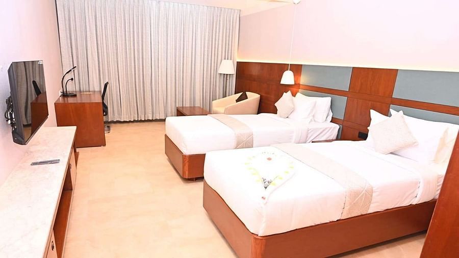 A Executive Suite at Dhanalakshmi Srinivasan Hotels, Perambalur featuring a neatly made twin beds with white linens and pillows, a wooden headboard, and a desk with a chair.