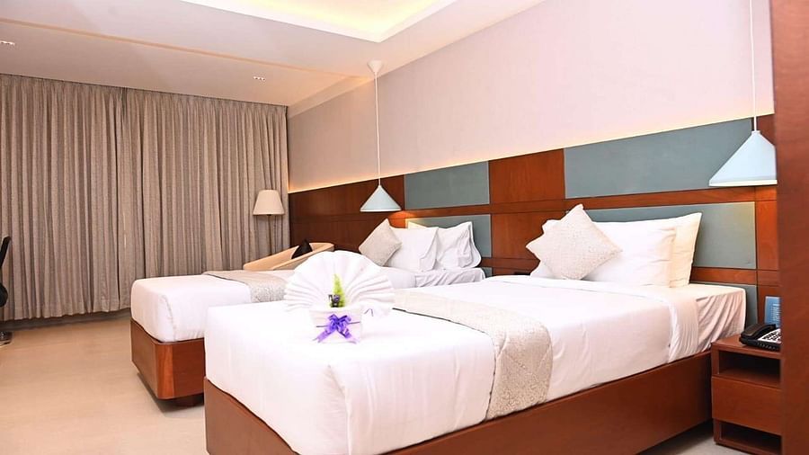 Side view of Executive Room at Dhanalakshmi Srinivasan Hotels, Perambalur featuring twin beds, furniture, and a window view. 