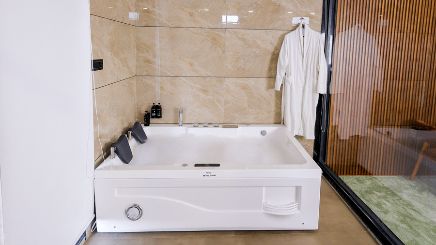 A modern bathroom featuring a white bathtub, glass shower enclosure, and neatly folded bathrobes.