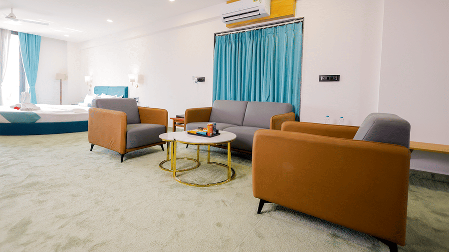 A bright suite with comfortable sofas, a coffee table, and turquoise curtains framing wide windows.