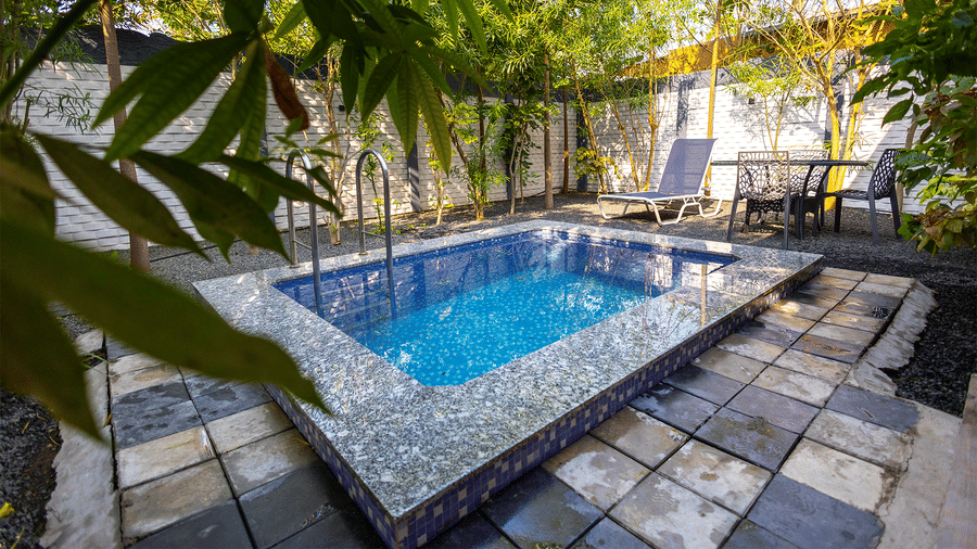 A small, inviting outdoor swimming pool features blue tiling and is surrounded by a paved patio area.