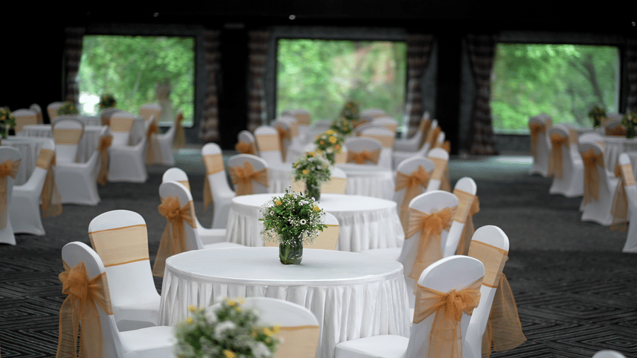 Banquet hall setup with round tables, white and gold chair covers, and floral centrepieces at Narayani Heights Hotel & Resorts, Ahmedabad.