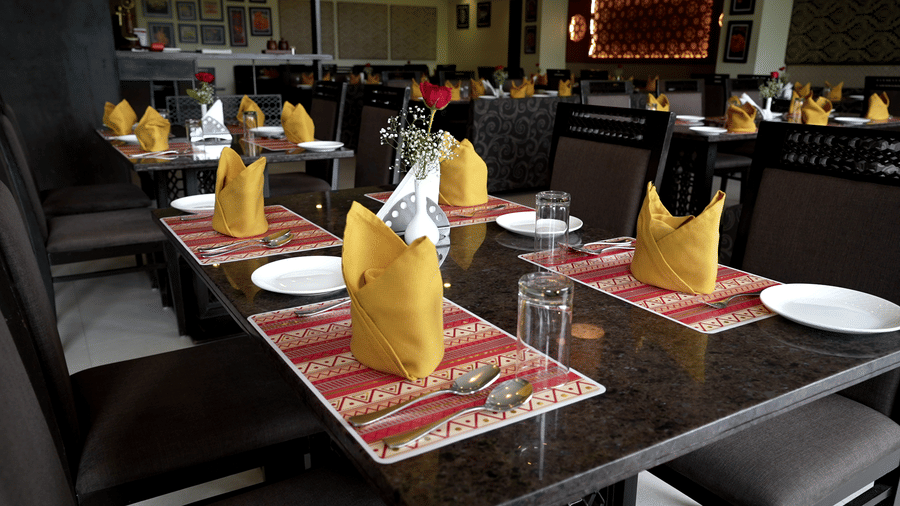 Close-up of a dining table set with folded napkins, cutlery, and tableware - Narayani Heights Hotel & Resorts