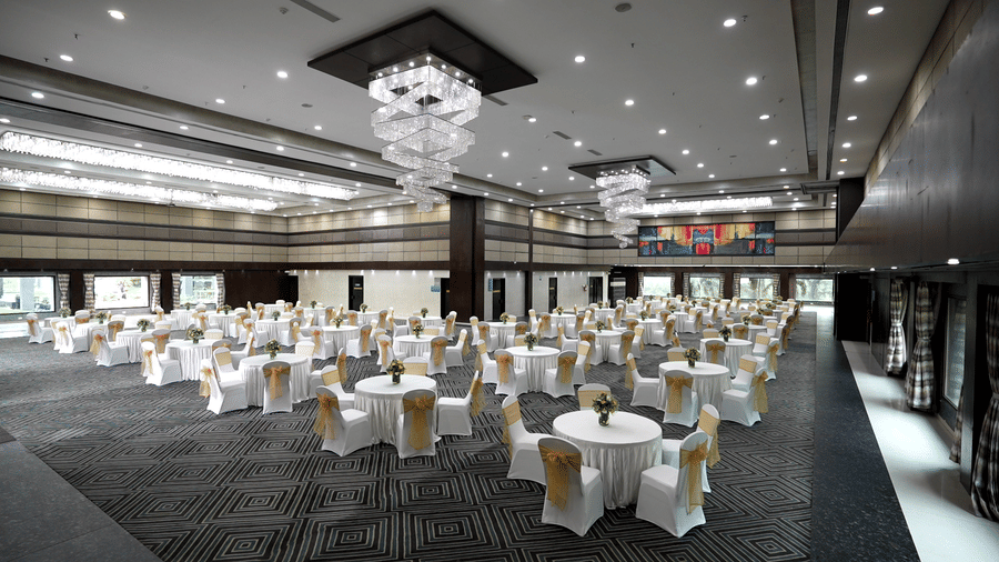 Spacious banquet hall with round tables and a chandelier ceiling - Narayani Heights Hotel & Resorts
