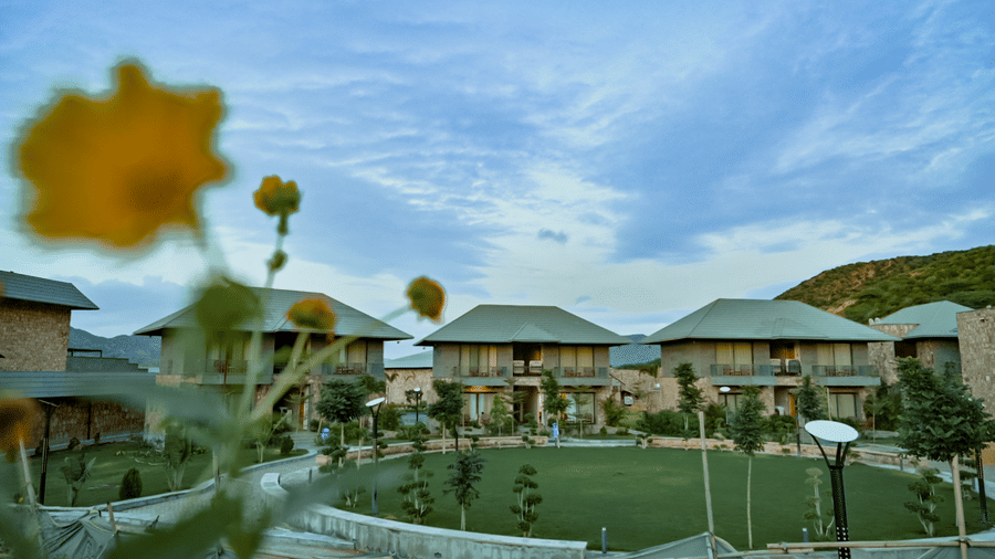 A wide view of several holiday villas and a manicured lawn at a resort, with a backdrop of green hills.