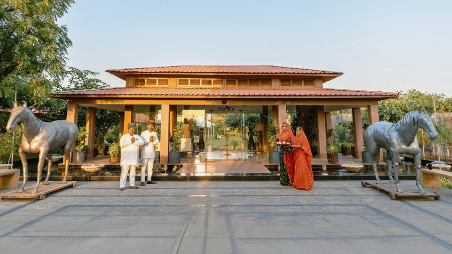 Staff in traditional attire at Surpura Bagh, Jodhpur welcome guests to a grand pavilion flanked by 2 large horse sculptures.