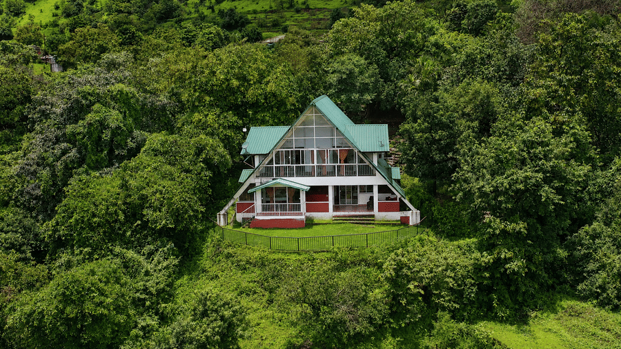 A frame chalet at Wind Chalet viewed from a distance, surrounded by dense forest and elevated greenery.