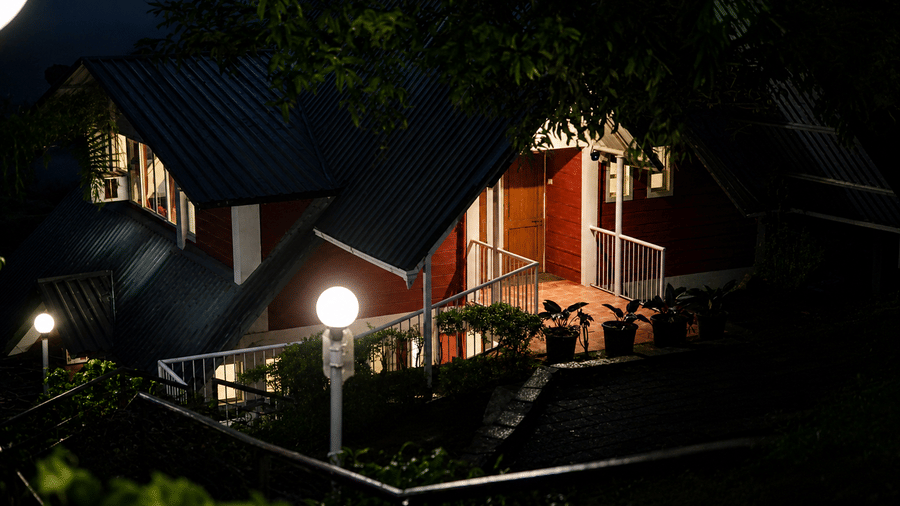 Wind Chalet illuminated at night, with an A frame chalet, covered outdoor walkway, entrance area, and surrounding trees visible under exterior lighting.