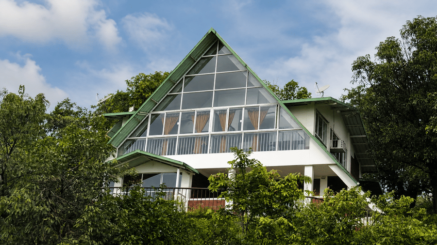 A frame chalet at Wind Chalet with a large glazed front section, steeply pitched roof, and dense greenery surrounding the building.