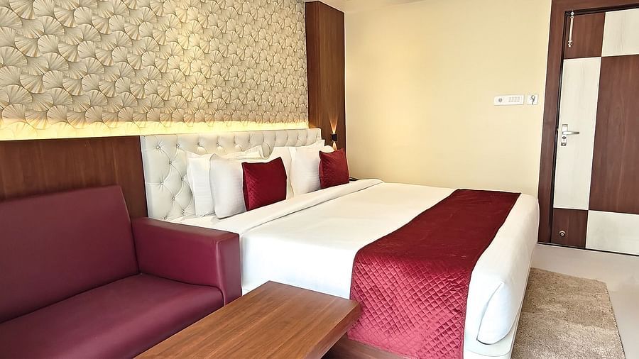 Deluxe Room furnished with a king size bed, a red sofa, and a wooden side table, all set against a textured grey wall at Yashshree Bangla Queen, Digha.