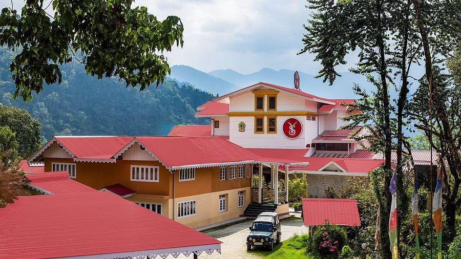 Charming hillside buildings with red rooftops set against a backdrop of lush green mountains under a partly cloudy sky - Yashshree Pelling Chekhim Retreat.