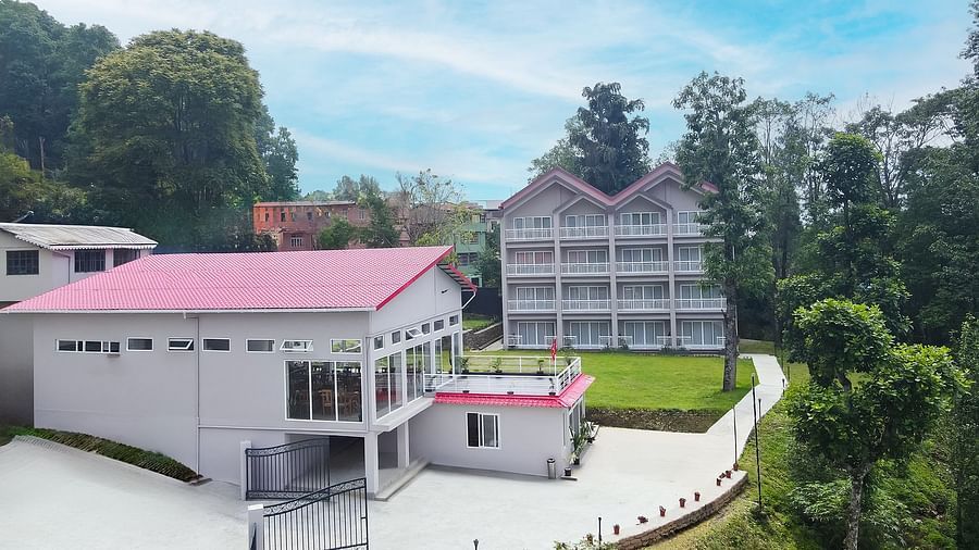 An aerial view of the buildings at Yashshree Resorts & Spa, Kalimpong, nestled amidst green hills and trees, with pathways leading between them.