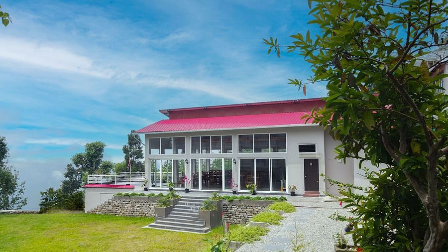 A modern hotel building at Yashshree Resorts & Spa, Kalimpong, with a distinctive red roof, set amidst lush greenery and a bright blue sky.