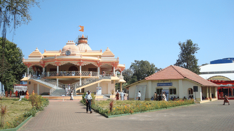 A wide shot of a beige building with a red-domed roof and a grassy lawn in front.