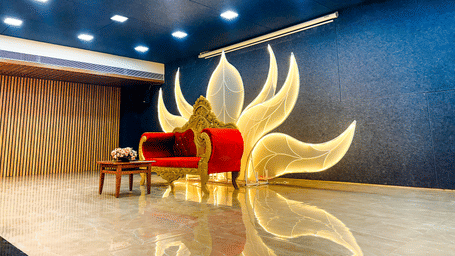 A regal red chair sits before a stunning, glowing, wing-shaped light display in an elegant and polished room.
