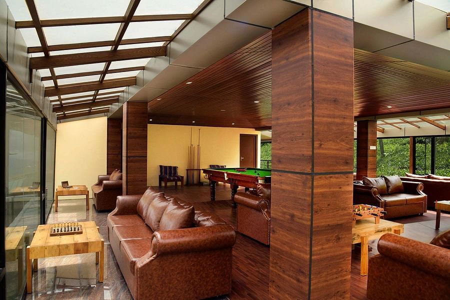 Shot of the indoor play area at the villa with brown sofas around Shot of the balcony at the villa with chairs kept | Ibex Stays and Trails, Valparai (Tale Rock)