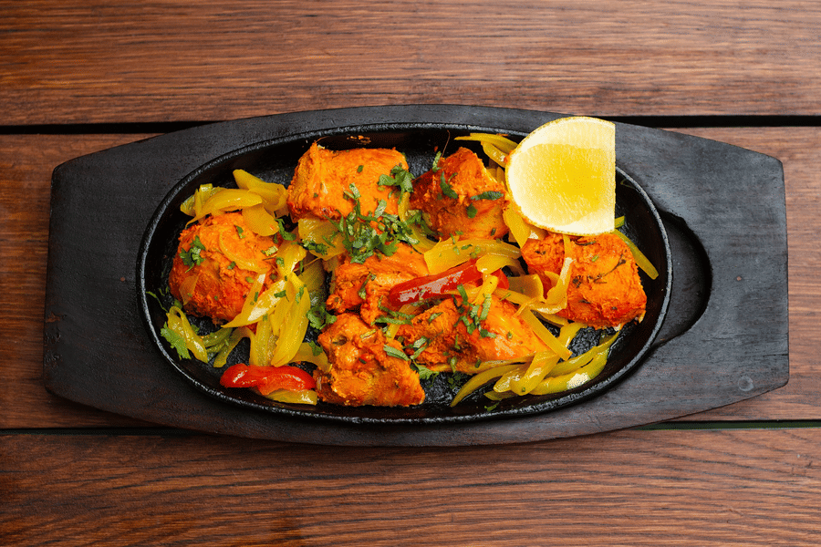 Scrumptious tandoori chicken beautifully platted and served with a piece of lemon and sorted veggies. 