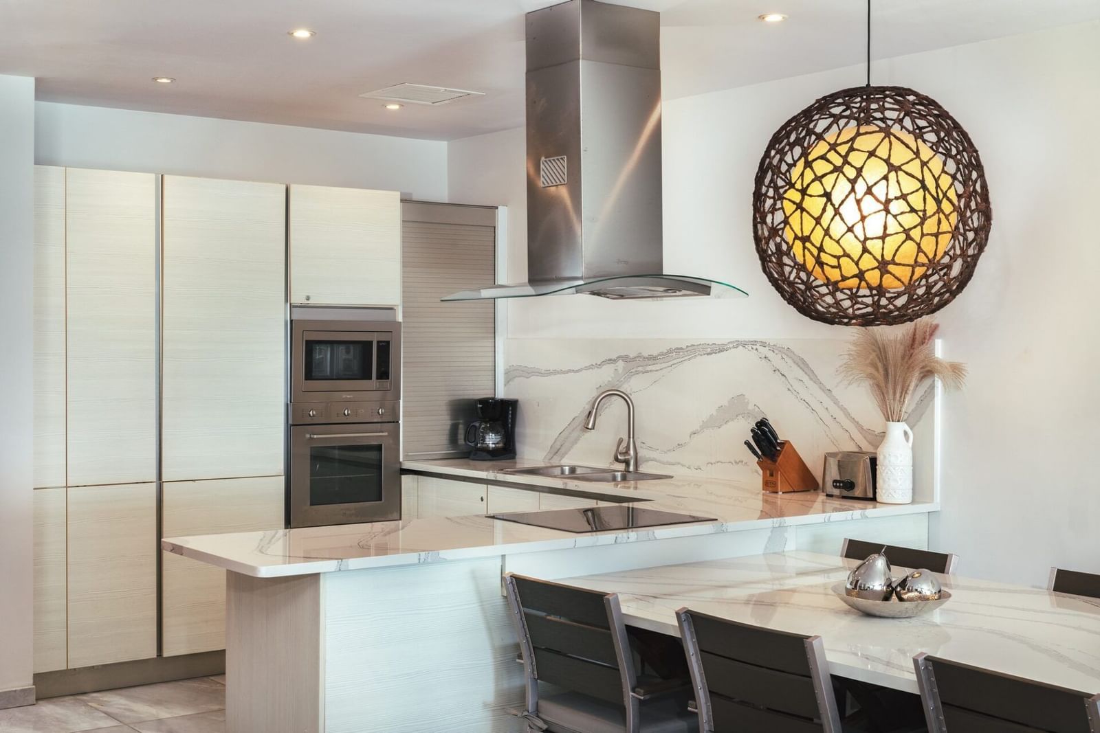 Contemporary kitchen with sleek white cabinetry, a central island with bar stools, and a statement pendant light.