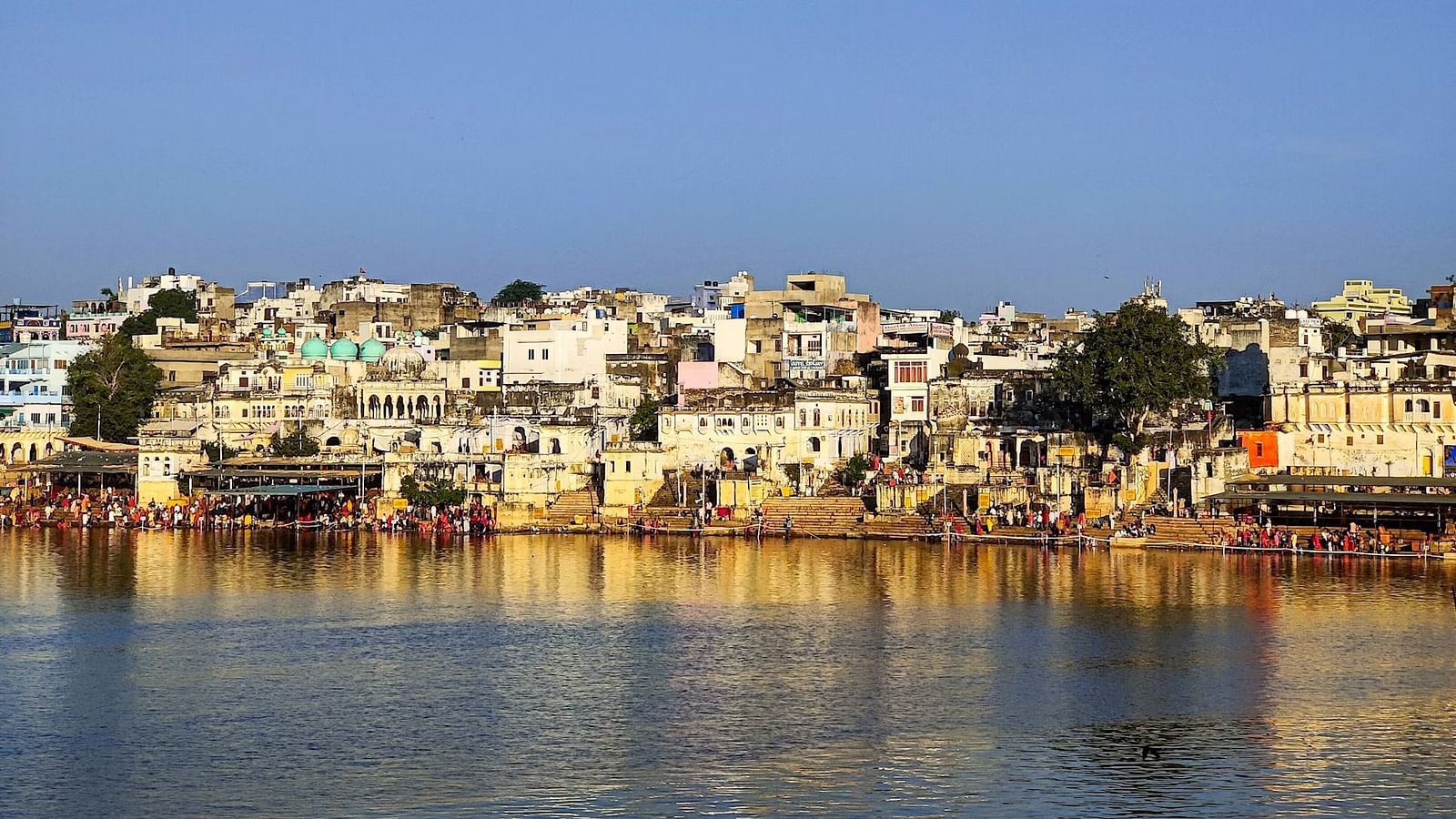 Buildings line the shore of a body of water under a clear sky.