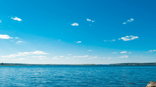 Serene view of a calm lake with clear blue skies and scattered clouds.