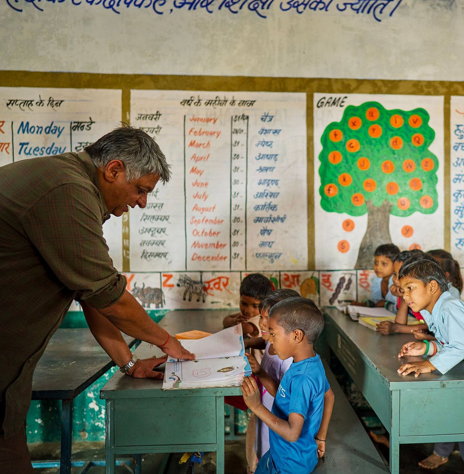 image of an old man teaching the children through a textbook at deogarh