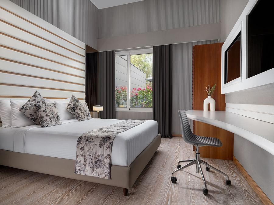 A chic room at The Atara, Gurugram with light wood flooring, a neatly made bed, a spacious desk with an office chair, and ample natural light from a large window
