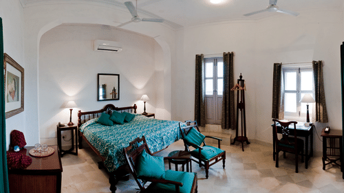 interior view of the Koel Mahal - Countryside View room with a king size bed draped in a teal bed cover.