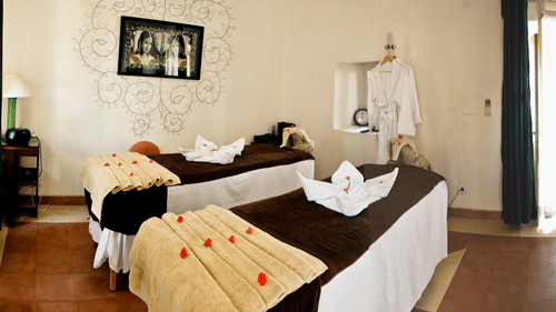 A spa room features two massage beds with towels and rose petals, along with robes and decor at Tijara Fort-Palace - 19th Century, Alwar.