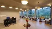 An indoor lounge area includes seating arrangements and pendant lighting, with a view of the outdoors. - Abad Brookside Lakkidi, Wayanad