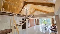 An attic room at Yashshree Resorts and Spa in Kalimpong featuring a wooden ceiling, a modern staircase to a loft, large windows leading to a balcony, and a seating area with two chairs.
