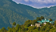 Facade of The Ramgarh Bungalows perched on a hill surrounded by scenic mountain view captured during the day.