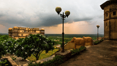 A view of Tijara Fort-Palace in Alwar shows its architecture, surrounding greenery, and an overcast sky.