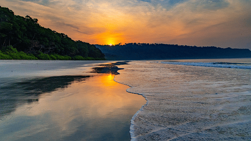 Radhanagar Beach during a sunset with the reflection of the sun on the water with shallow waves crashing the shore