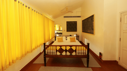 The Tower House - The Moens room with yellow curtains and a queen size bed with wall paintings 2