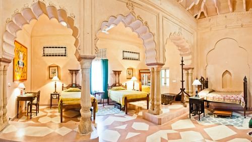 Arched openings define the different sleeping and living spaces within a suite at Tijara Fort-Palace - 19th Century, Alwar, featuring multiple beds and seating areas.