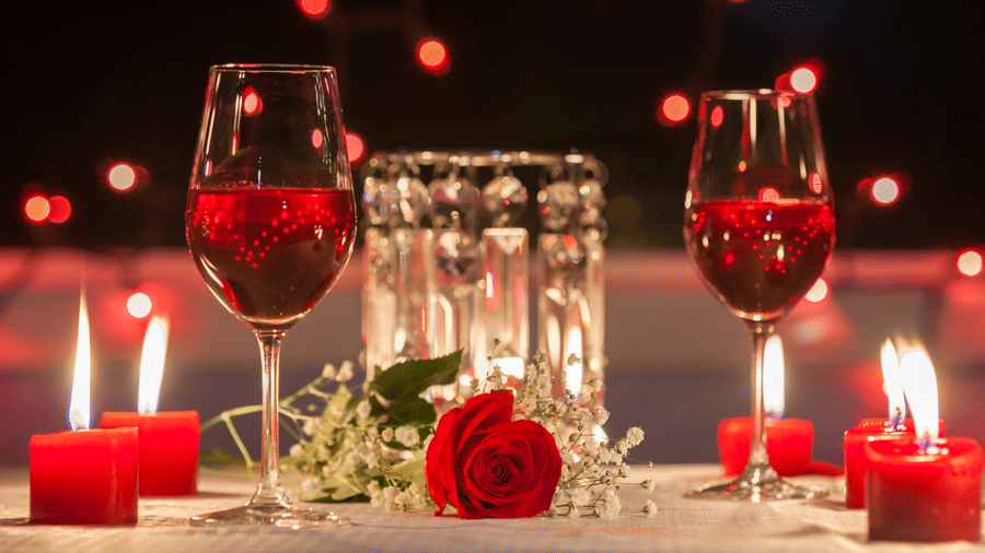 Candlelit Valentine dinner setup with wine glasses, red roses and glowing candles in a romantic ambiance.