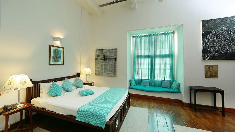 The Tower House - The Braganza room with light blue lines and pillows and a white walls. The room also features a queen size bed and bedside lamp
